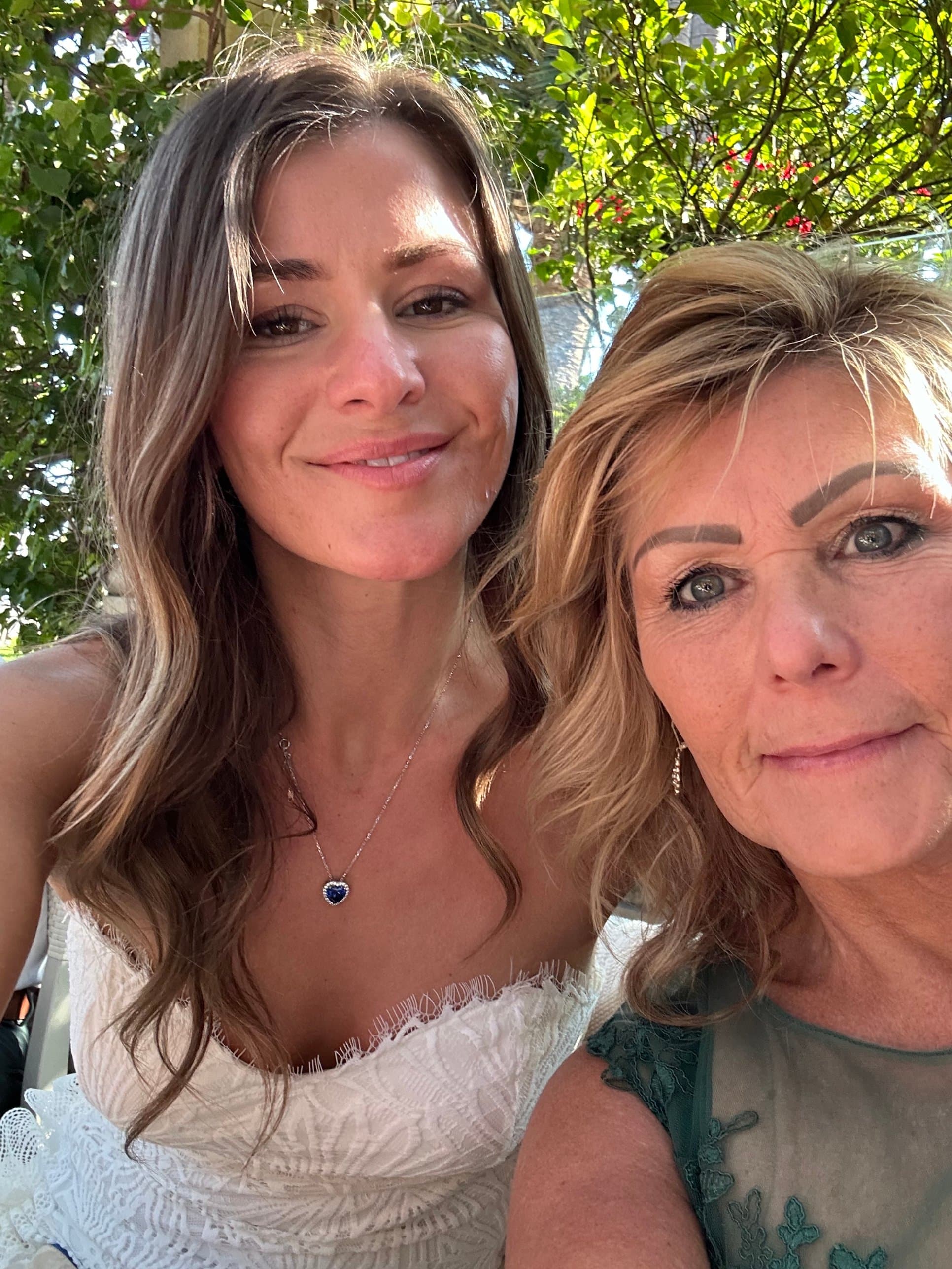 Selfie of Mary Leeds and her daughter smiling together outdoors in front of green leafy trees